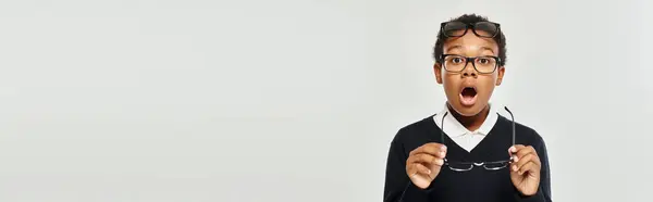 Schockierter afrikanisch-amerikanischer Junge in Pullover und Brille mit Brille und Blick in Kamera, Banner — Stockfoto
