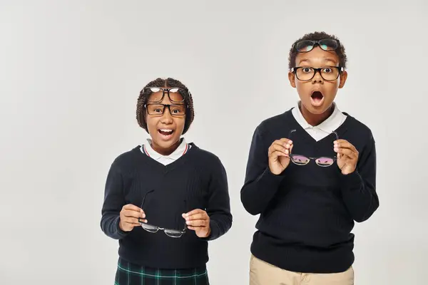 Изумленные и удивленные африканские американские школьники в очках на сером фоне, реакция — стоковое фото