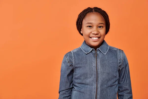 Portrait of happy african american girl with braids smiling and looking at camera on orange backdrop — Stock Photo