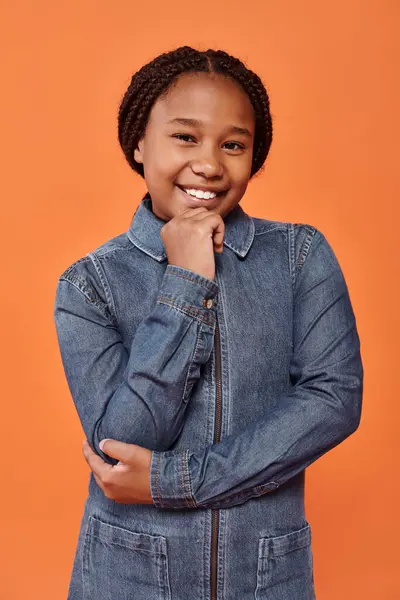 Positive afro-américaine fille avec des tresses souriant et regardant la caméra sur fond orange — Photo de stock
