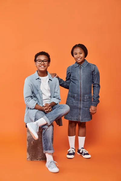 Joyeux enfants afro-américains en tenue décontractée en denim posant ensemble sur fond orange — Photo de stock