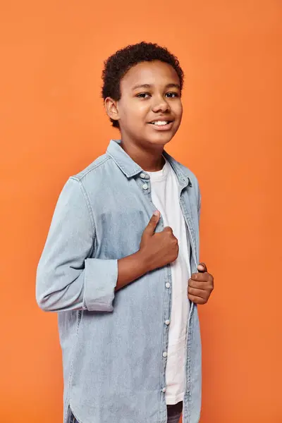 Joyous african american boy in casual outfit posing happily and smiling at camera on orange backdrop — Stock Photo