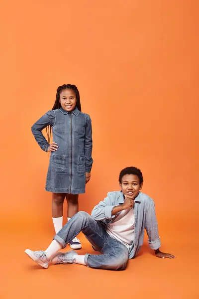 Cheerful african american boy and girl posing together on orange backdrop and smiling at camer — Stock Photo