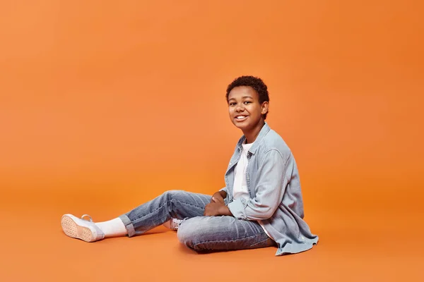 Joyous african american boy in casual attire sitting on floor and smiling cheerfully at camera — Stock Photo