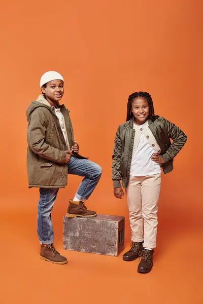 Alegre preadolescente afroamericano amigos en invierno trajes posando juntos en naranja telón de fondo - foto de stock