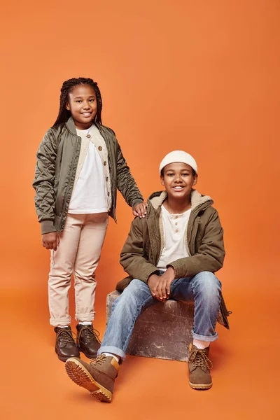 Cheerful preadolescent african american boy and girl in winter attire posing on orange backdrop — Stock Photo