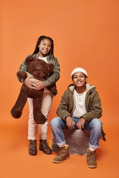 Cheerful preadolescent african american kids posing with teddy bear and smiling happily at camera — Stock Photo