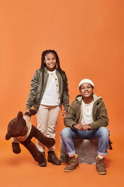 Joyous preteen african american girl with braids and boy with beanie hat smiling at camera — Stock Photo