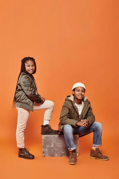Preteen cheerful african american friends in winter outfits posing together on orange backdrop — Stock Photo
