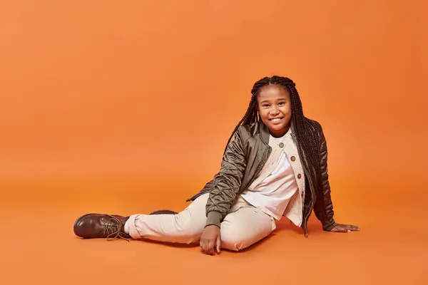Alegre pré-adolescente afro-americana menina em trajes quentes de inverno sentado no chão e sorrindo para a câmera — Fotografia de Stock