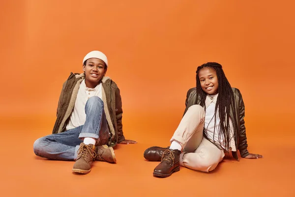 Allegro preteen africani amici americani in abiti caldi seduti sul pavimento e sorridente felicemente — Foto stock