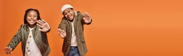 Alegres crianças afro-americanas em roupas quentes posando em movimento e sorrindo para a câmera, banner — Fotografia de Stock