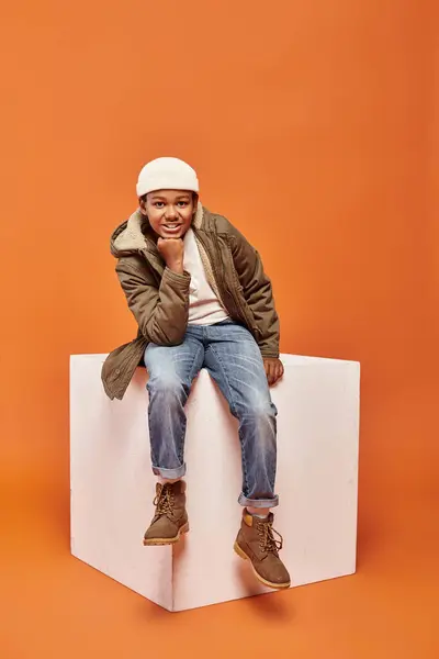Feliz preadolescente afroamericano chico en abrigo de invierno caliente y gorro sombrero sonriendo alegremente a la cámara - foto de stock