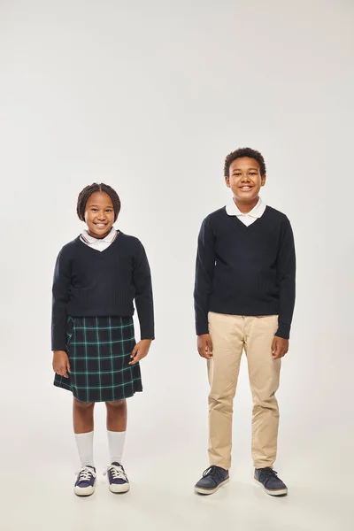 Felice afro-americano scolaresche in uniforme posa insieme su sfondo grigio e sorridente alla macchina fotografica — Foto stock