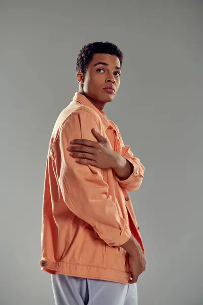 Hombre guapo en camisa de melocotón de pie contra la pared gris, sentido de la moda que muestra su personalidad - foto de stock