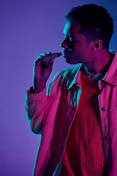 Африканский американец кипит с электронной сигаретой в руке, серый фон с освещением — стоковое фото
