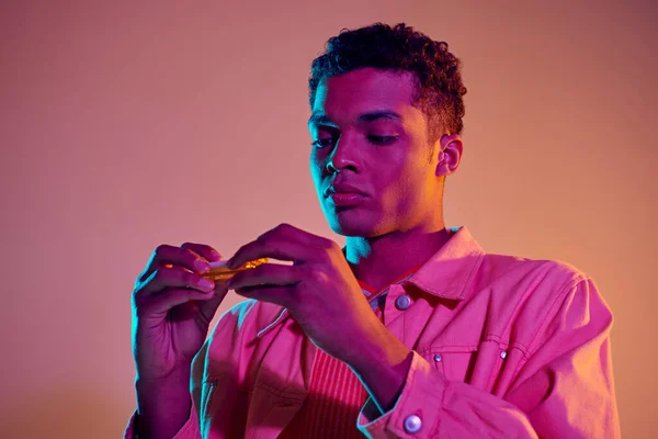 African american man preparing e-cigarette on vibrant background with blue neon lighting — Stock Photo