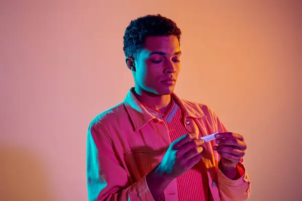 Afrikanischer Amerikaner dreht Zigarette zum Rauchen auf buntem Hintergrund mit blauer Neonbeleuchtung — Stockfoto