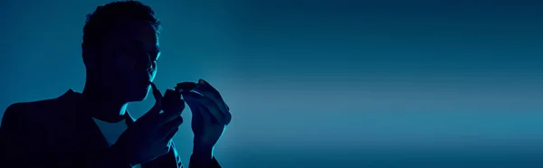 Pancarta, hombre afroamericano sosteniendo más ligero mientras fuma pipa sobre fondo azul oscuro con iluminación - foto de stock