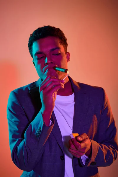 Afrikanisch-amerikanischer Mann mit Zigarre Streichholz mit Feuer auf rosa Hintergrund mit blauer Beleuchtung — Stockfoto