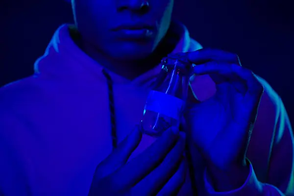 Homem americano africano cultivado com capuz segurando jarra com cannabis medicinal em azul escuro em torno de fumaça — Fotografia de Stock