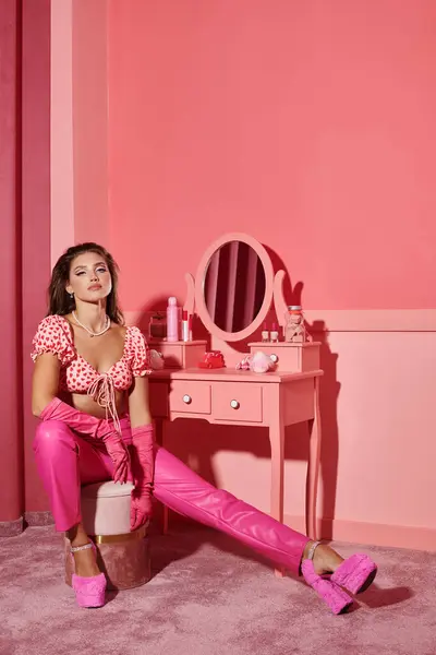 Bela e jovem mulher no topo da colheita e calças sentadas perto da mesa da vaidade com espelho no quarto rosa — Fotografia de Stock