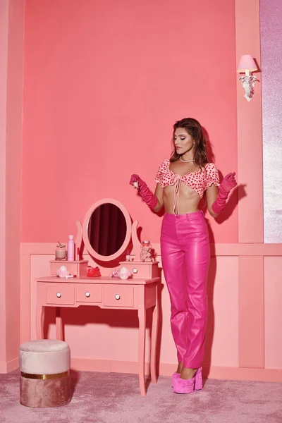 Beautiful young woman in pink attire holding nail polish bottle near vanity table with mirror — Stock Photo
