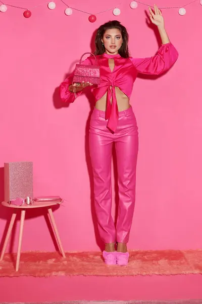 Poupée glamour comme une femme en haut de culture et pantalon rose debout avec sac à main près guirlande de balle — Photo de stock