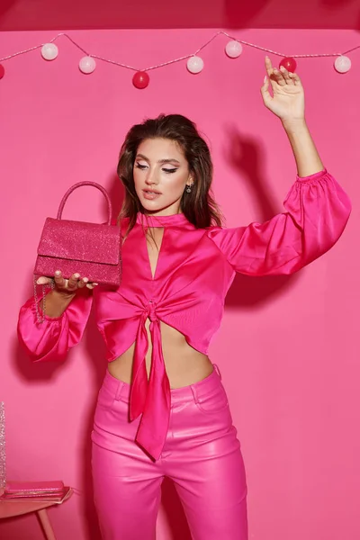 Boneca bonita como mulher no topo da colheita e calças rosa de pé com bolsa chique perto de grinalda bola — Fotografia de Stock