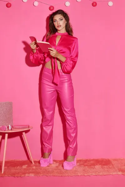 Belle poupée comme une femme en haut de culture et pantalon rose debout avec livre près de guirlande de balle — Photo de stock