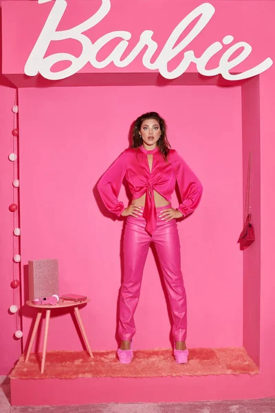 KYIV, UCRANIA - 14 de julio de 2023: Muñeca sorprendida como una mujer en top de la cosecha y pantalones de color rosa de pie con las manos en las caderas en la habitación de color rosa, Barbie - foto de stock