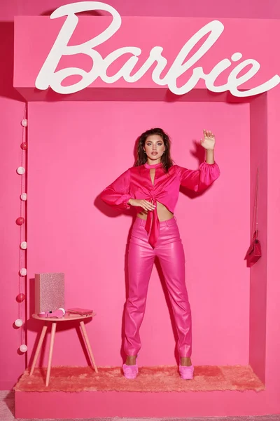 KYIV, UCRANIA - 14 de julio de 2023: mujer joven y bonita en top de la cosecha y pantalones de color rosa haciendo un gesto antinatural y actuando como una muñeca, Barbie - foto de stock
