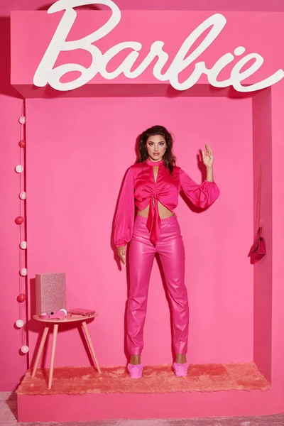 KYIV, UCRANIA - 14 de julio de 2023: seductora joven en top de cosecha y pantalones rosados que hacen gestos antinaturales y actúan como una muñeca Barbie - foto de stock