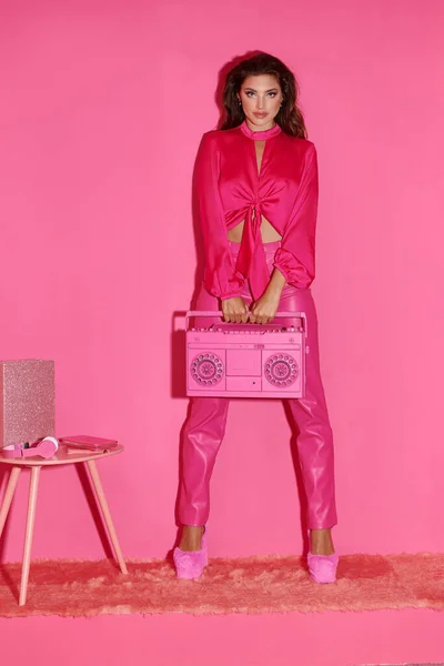 Hermosa mujer joven con el pelo rizado de pie en vibrante traje rosa sosteniendo boombox retro - foto de stock