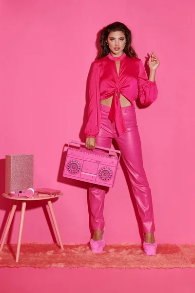 Hermosa mujer joven con el pelo rizado posando en traje rosa vibrante y sosteniendo boombox retro - foto de stock