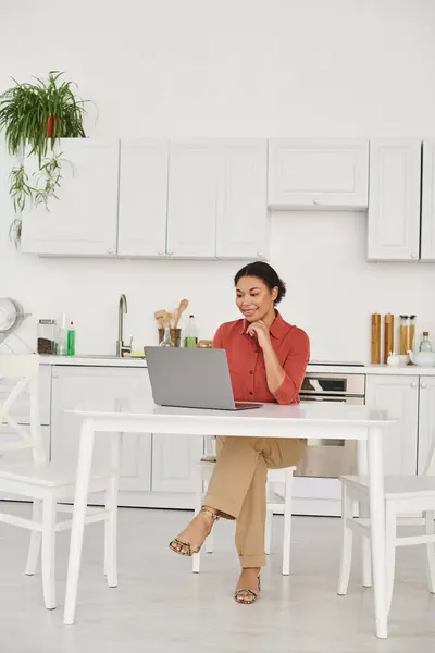 Remote working of happy young african american nutritionist using laptop in her kitchen, woman — Stock Photo
