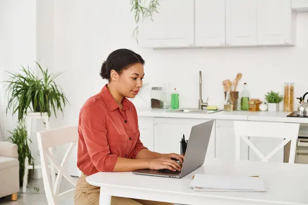 Focused african american nutritionist using laptop while working remotely from her modern kitchen — Stock Photo