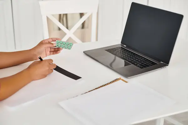 Cropped view of dietitian holding medication during online consultation on laptop from her kitchen — Stock Photo