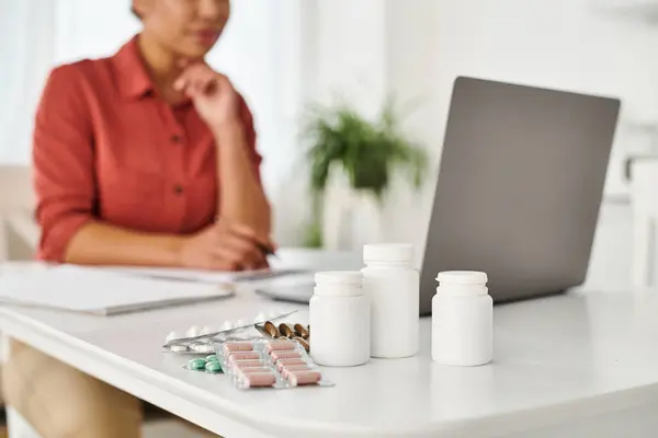 Лекарства в бутылках и пузырьках на столе рядом с размытым диетологом, онлайн консультация — стоковое фото