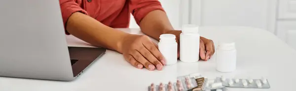 Vista recortada de dietista afroamericano cerca de botellas con diferentes medicamentos en la mesa, pancarta - foto de stock