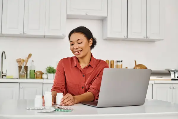 Happy nutritionist looking at bottles with different medication during online consultation on laptop — Stock Photo