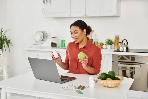 Nutricionista afroamericano sosteniendo manzana y suplementos mientras que ofrece consejos de salud en línea - foto de stock
