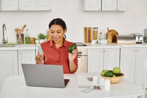 Nutricionista afro-americano segurando abacate e suplementos, dando conselhos de dieta de laptop — Fotografia de Stock