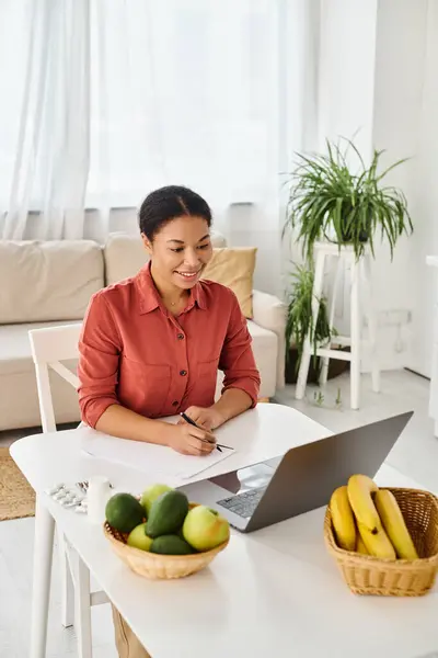 Nutricionista afroamericano feliz tomando notas mientras mira el portátil durante la consulta en línea - foto de stock
