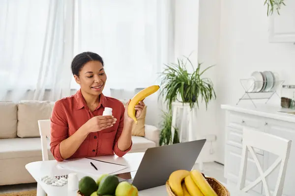 Nutricionista afroamericano feliz sosteniendo manzana y dando consejos de dieta en el ordenador portátil en la cocina - foto de stock