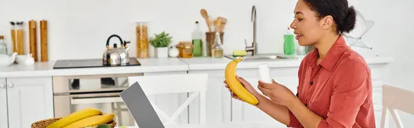 Feliz nutricionista afro-americano segurando banana e dando conselhos de dieta no laptop, banner — Fotografia de Stock