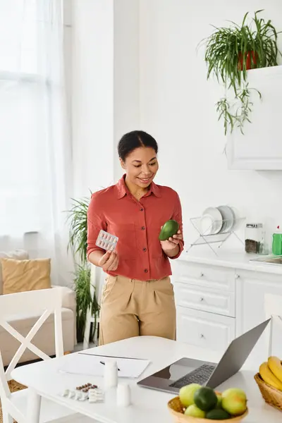 Счастливый африканский американский диетолог держит спелый авокадо и дает советы по диете на ноутбуке на кухне — стоковое фото