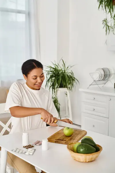 Nutricionista afroamericano alegre compara suplementos con frutas para una dieta saludable en el hogar - foto de stock