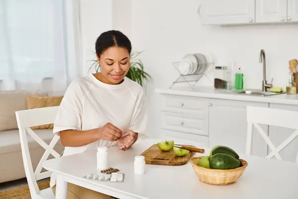 Happy african american nutritionist compares supplements with fruits for a healthy diet at home — Stock Photo