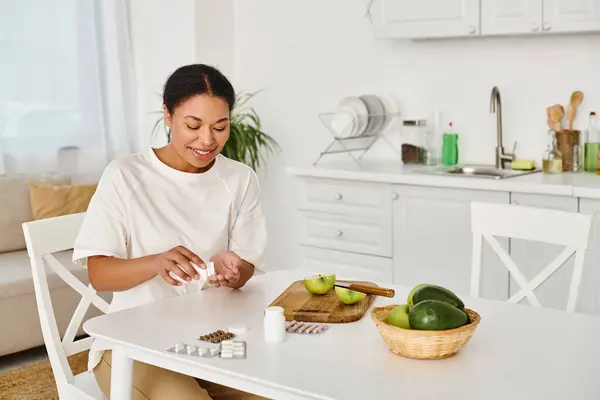 Nutricionista afro-americano satisfeito compara suplementos com frutas para uma dieta saudável em casa — Fotografia de Stock